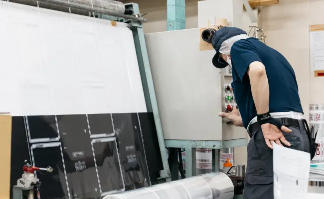 フィルム巻き返し検査機で印刷フィルムの品質を確認する作業員